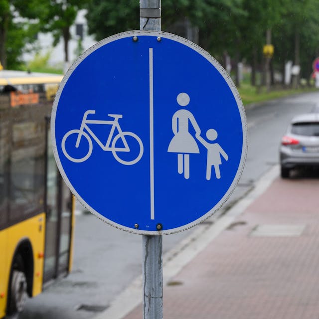 Ein Schild für einen getrennten Rad- und Gehweg steht vor dem Ende eines Radweges und dem Beginn der Zone, in der das Parken auf dem halben Gehweg erlaubt ist.