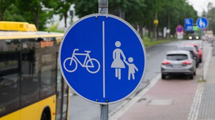 Ein Schild für einen getrennten Rad- und Gehweg steht vor dem Ende eines Radweges und dem Beginn der Zone, in der das Parken auf dem halben Gehweg erlaubt ist.