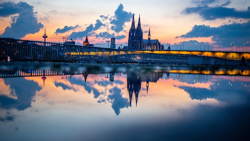 Das Stadtpanorama mit dem Kölner Dom spiegelt sich am Abend kurz vor 22 Uhr in einer Regenpfütze auf der Deutzer Werft.