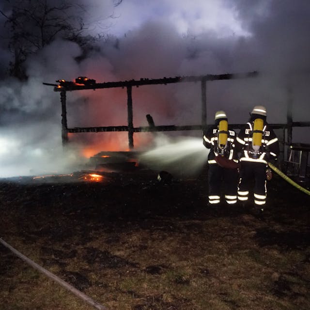 Das Bild zeigt, wie Feuerwehrleute die Flammen mit Wasser bekämpfen.
