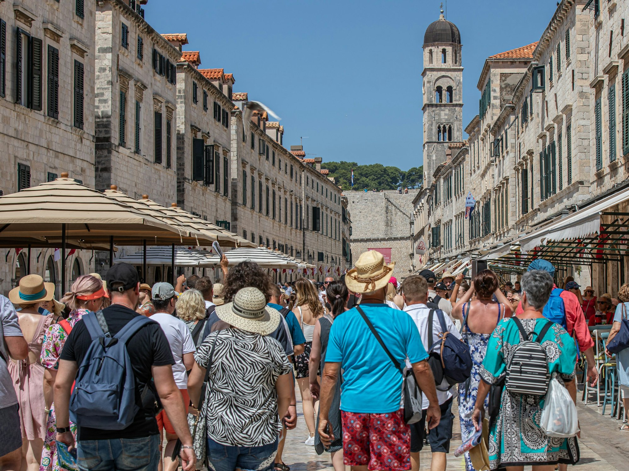 Touristen gehen an dem heißen Tag durch eine Geschäftsstraße von Dubrovnik.