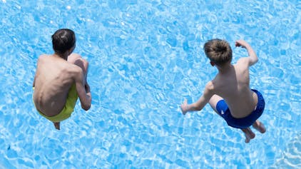 Zwei Jungen springen im Freibad ins Wasser.&nbsp;