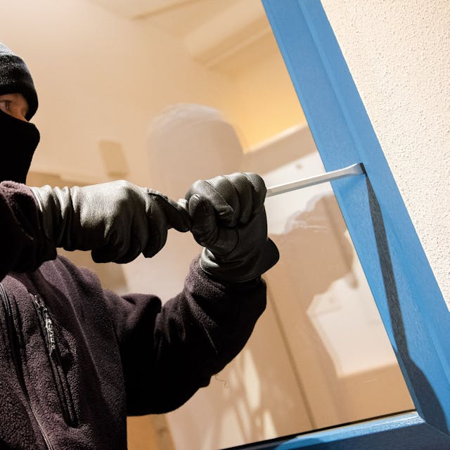 Ein als Einbrecher verkleideter Mann hebelt in einer Kriminalpolizeilichen Beratungsstelle der Polizei ein Fenster auf.
