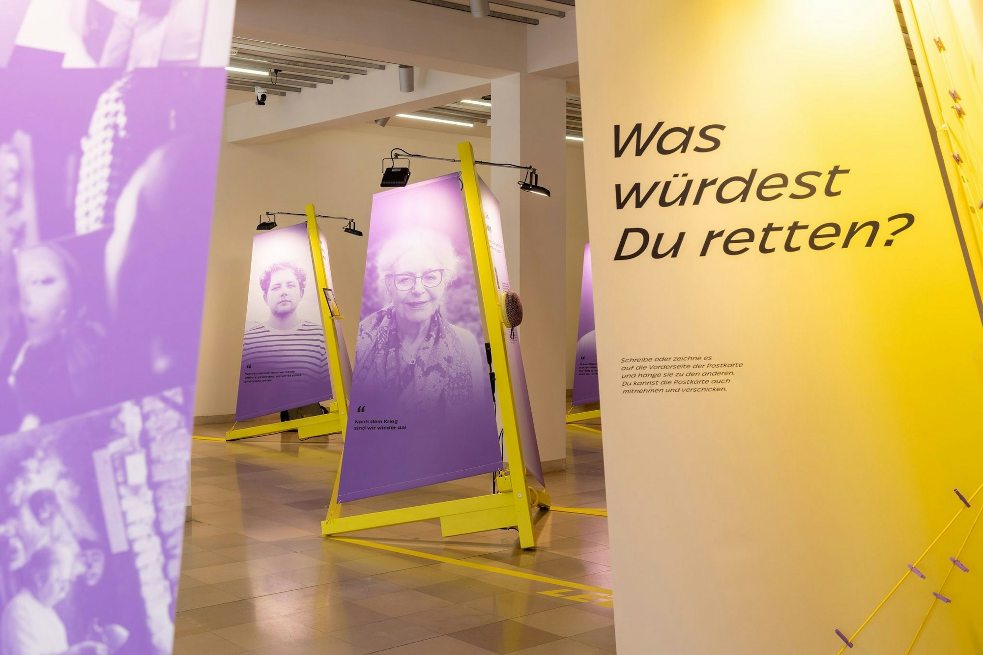Das Bild zeigt die Ausstellung. Violette Segeln hängen an gelben Masten und zeigen die Kulturretter. Im Vordergrund steht ein Segel mit der Aufschrift: „Was würdest du retten?“.