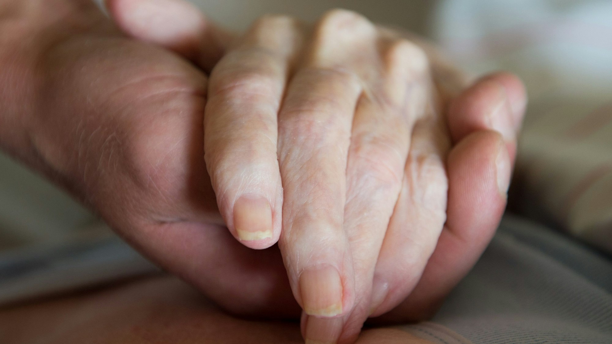 Ein Altenpfleger hält in einem Pflegeheim die Hand einer Frau.