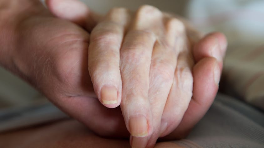 Ein Altenpfleger hält in einem Pflegeheim die Hand einer Frau.