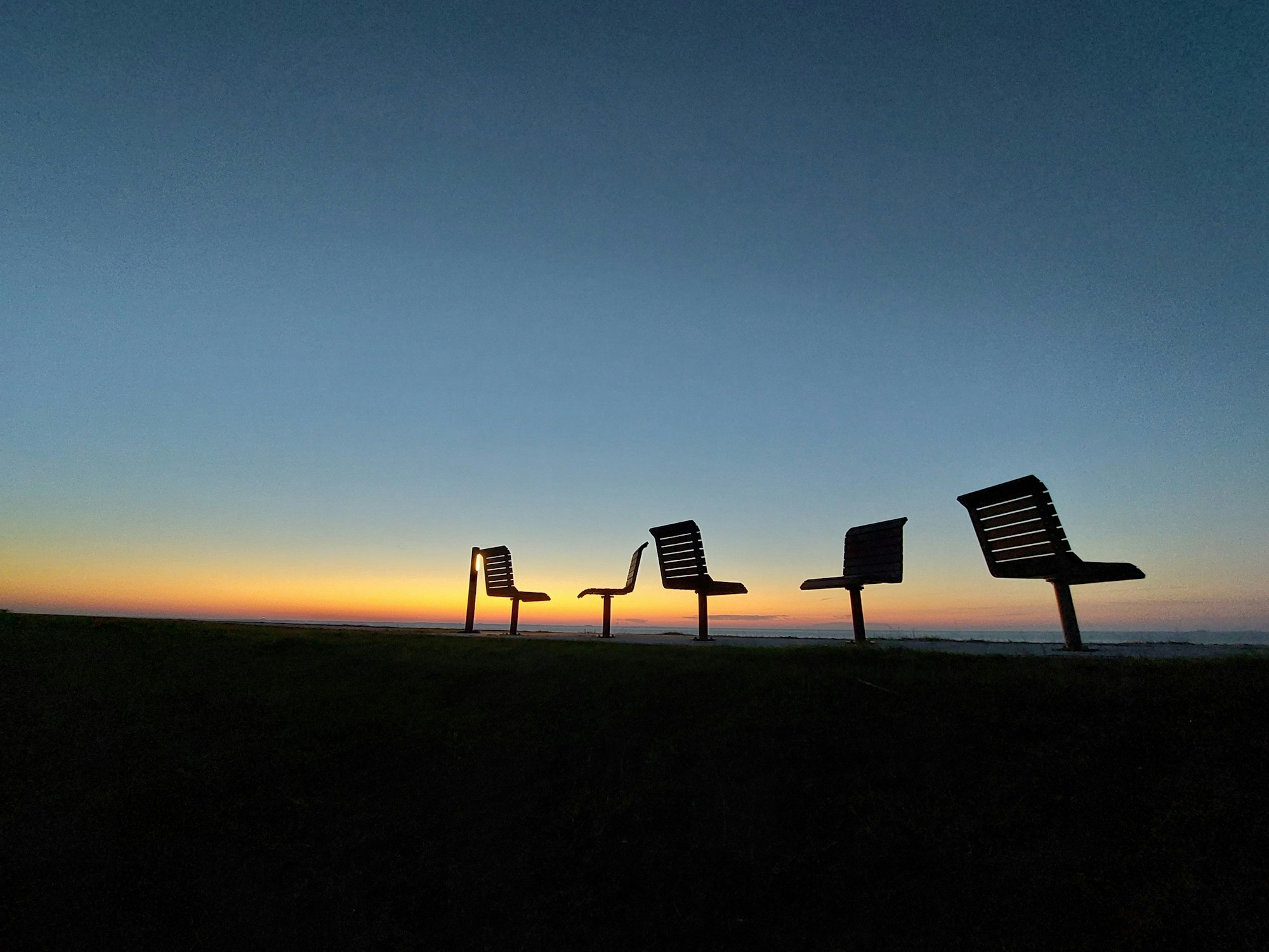 Das Foto zeigt verlassene Sitzgelegenheiten an der Promenadeauf der Halbinsel Nordstrand an der Nordseeküste beim Sonnenuntergang.