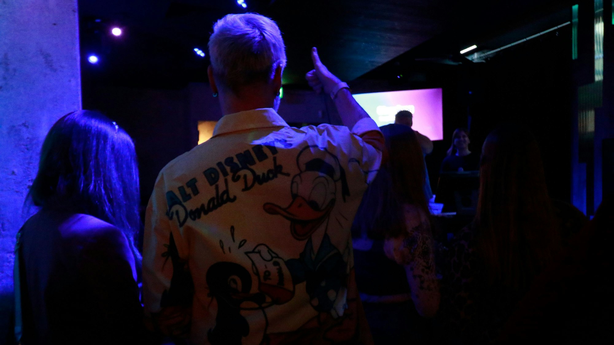 Zwei Personen stehen in einer Menge. Ein Mann trägt ein Hemd mit Disney-Motiv.