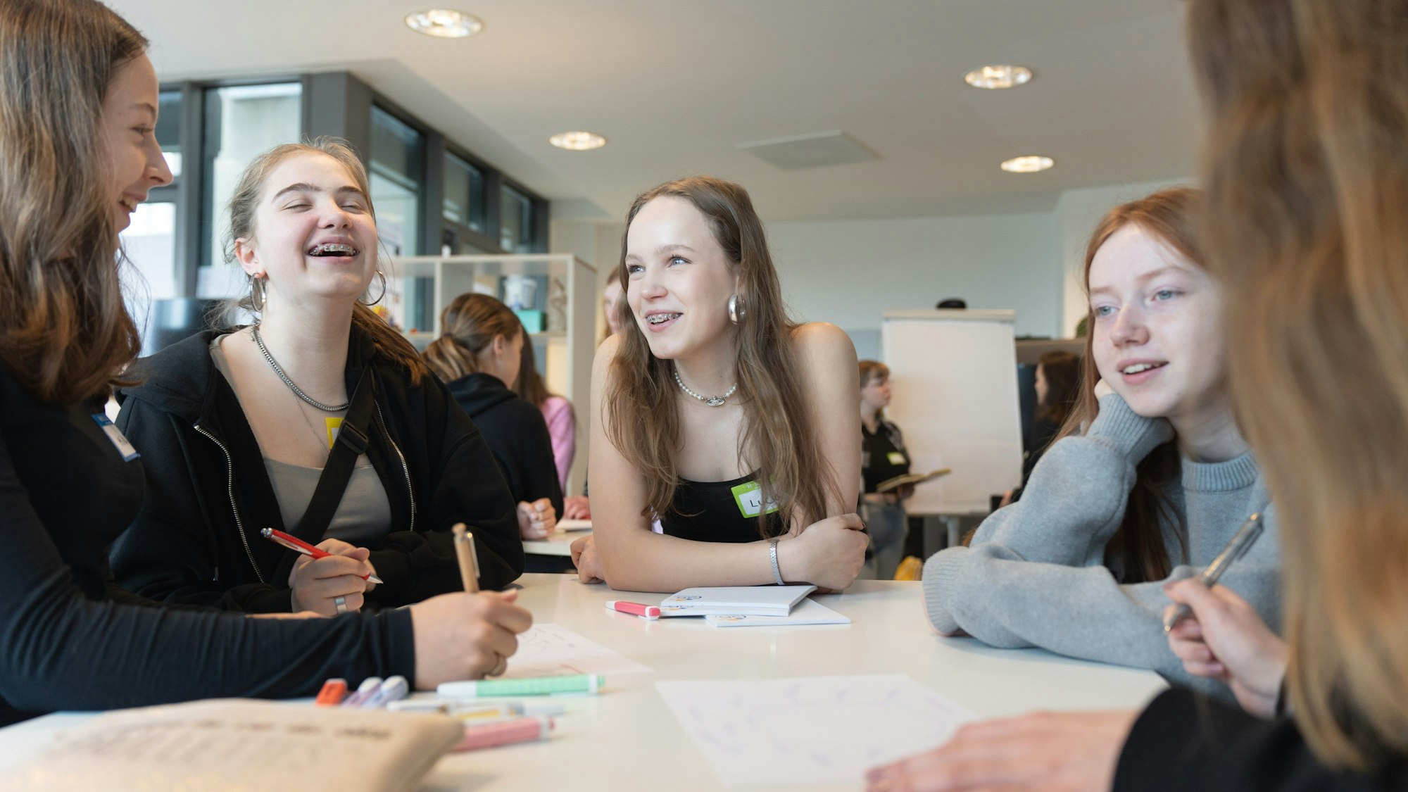 Fünf Mädchen stehen um einen Tisch und brainstormen Ideen für Unternehmensgründungen.