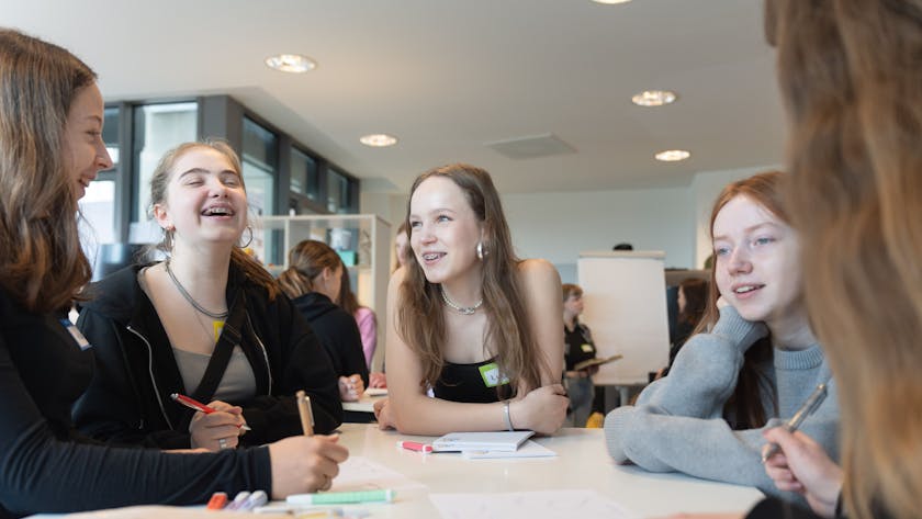 Fünf Mädchen stehen um einen Tisch und brainstormen Ideen für Unternehmensgründungen.