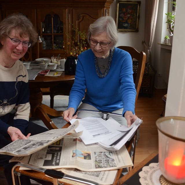 Zwei Seniorinnen blicken auf alte Zeitungsberichte.