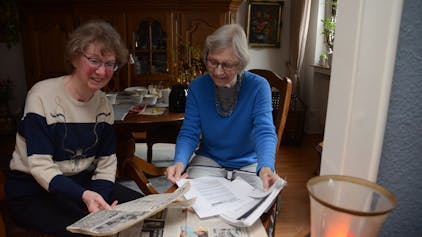 Zwei Seniorinnen blicken auf alte Zeitungsberichte.