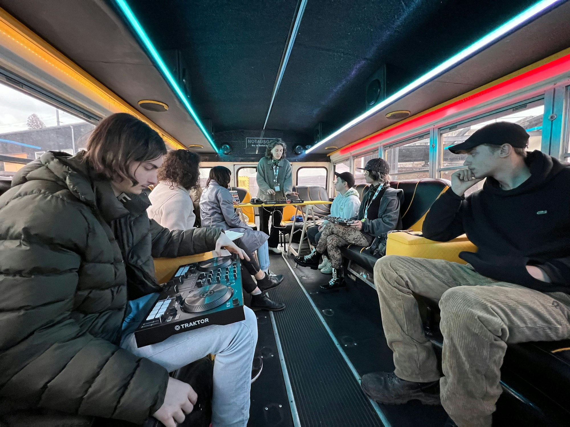 Menschen sitzen im zum Partybus umgebauten Schulbus, wo ein Workshop zum Auflegen von Musik stattfindet