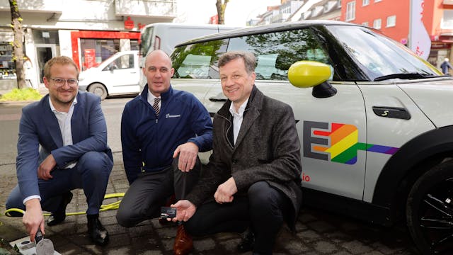 Drei Männer knien vor einem E-Auto, das an einer neuen Ladestation geladen wird.