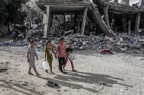 25.04.2024, Palästinensische Gebiete, Rafah: Inmitten des anhaltenden Konflikts zwischen Israel und der islamistische Hamas gehen palästinensische Kinder neben einem zerstörten Haus nach einem israelischen Luftangriff.