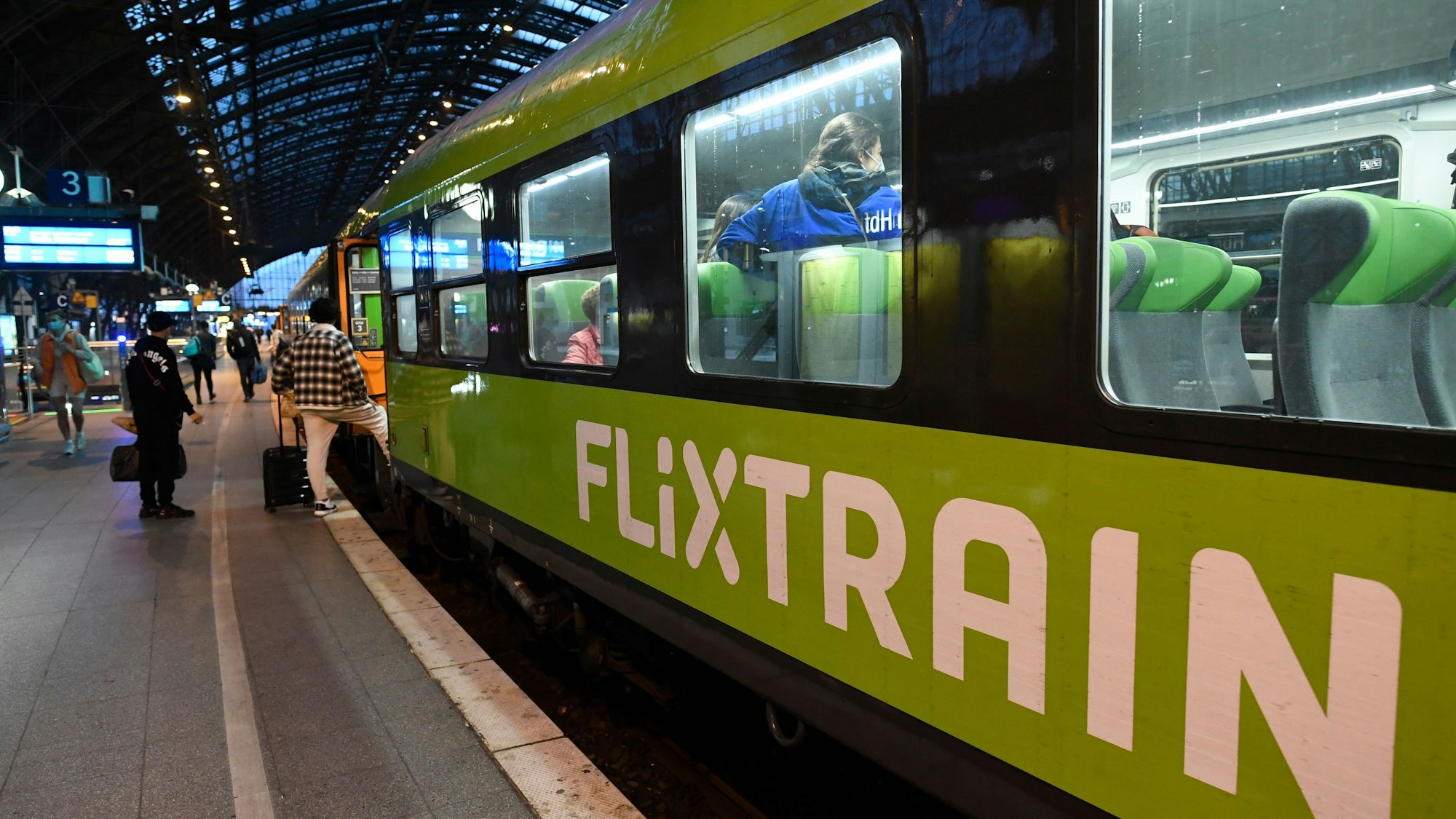 Mehrere Reisende steigen in einen Flixtrain am Kölner Hauptbahnhof, der Zug ist markant grün lackiert. Im Innenraum sind mehrere Fahrgäste zu sehen.
