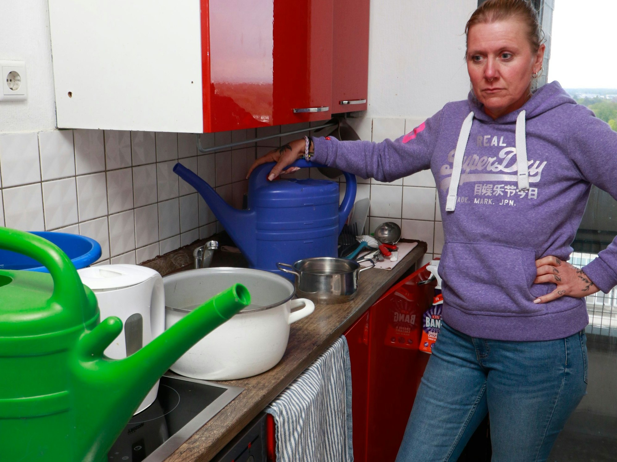 Eine Frau steht vor einer Küche, auf der Gießkannen und Töpfe sind.
