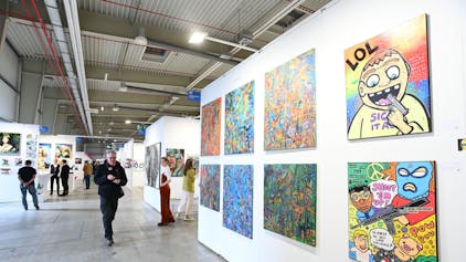 Das Treiben auf der Kunstmesse Discovery Art Fair 2024 am 25.04.2024 in Köln. Im Vordergrund sind bunte Pop-Art-Werke zu sehen. Foto von Alexander Schwaiger.