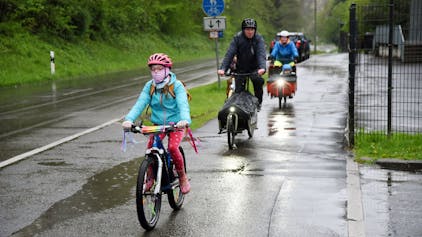 Kinder und Erwachsene auf Fahrrädern fahren entlang einer nassen Straße.