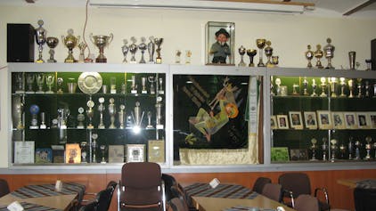 Das Bild zeigt die große Pokalvitrine der Hubertus-Schützen mit zahlreichen Trophäen, Standartentuch, Urkunden und Porträtfotos.