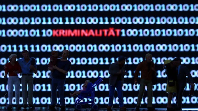 Modellfiguren stehen vor einem Computerbildschirm mit Zeichen des Binärcodes und dem Schriftzug "Kriminalität"