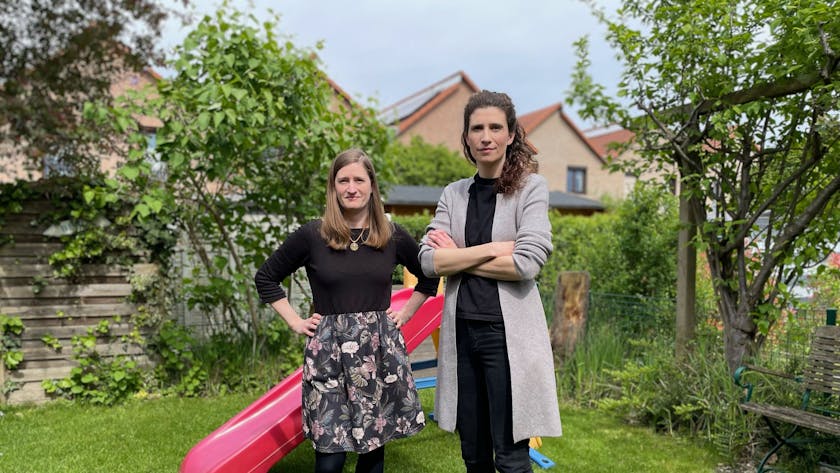 Zwei Frauen in einem Garten; im Hintergrund steht eine bunte Kinderrutsche aus Kunststoff.