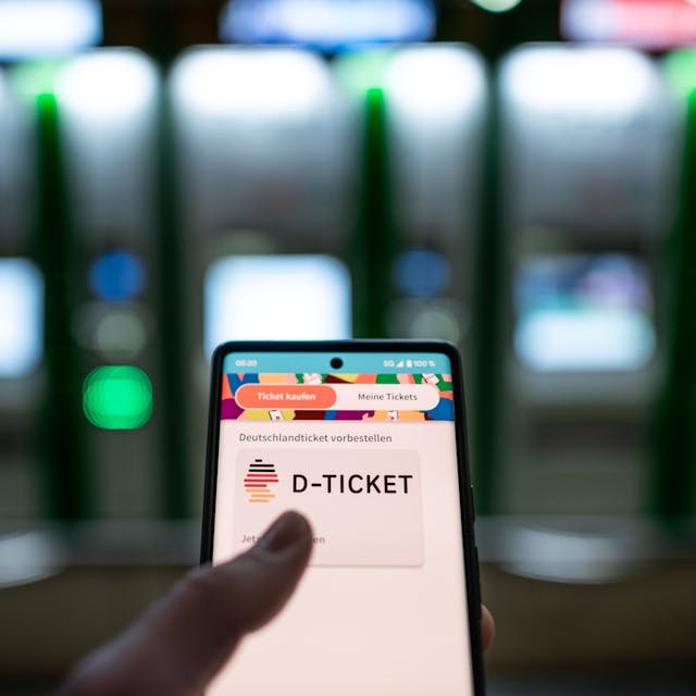 Ein Mann hält ein Mobiltelefon, auf dem das „D-Ticket“ gekauft werden kann, vor Ticketautomaten am Hauptbahnhof in der Hand.