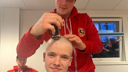 Ein junger Mann rasiert einem anderen jungen Mann die Kopfhaare ab.