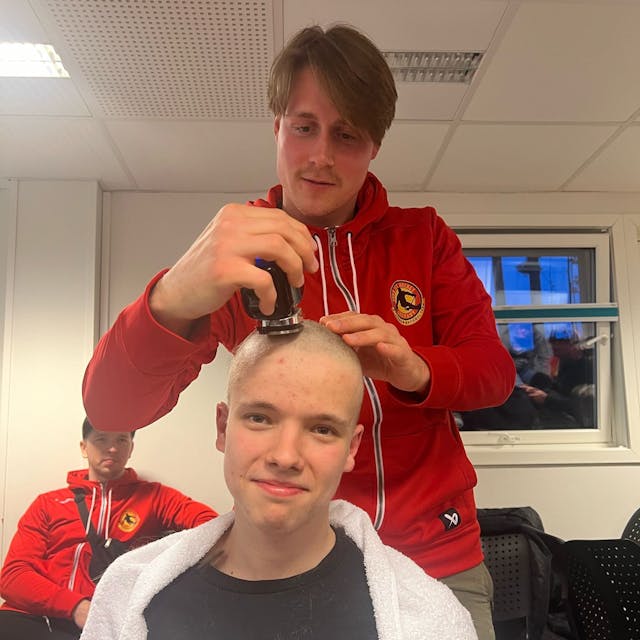Ein junger Mann rasiert einem anderen jungen Mann die Kopfhaare ab.