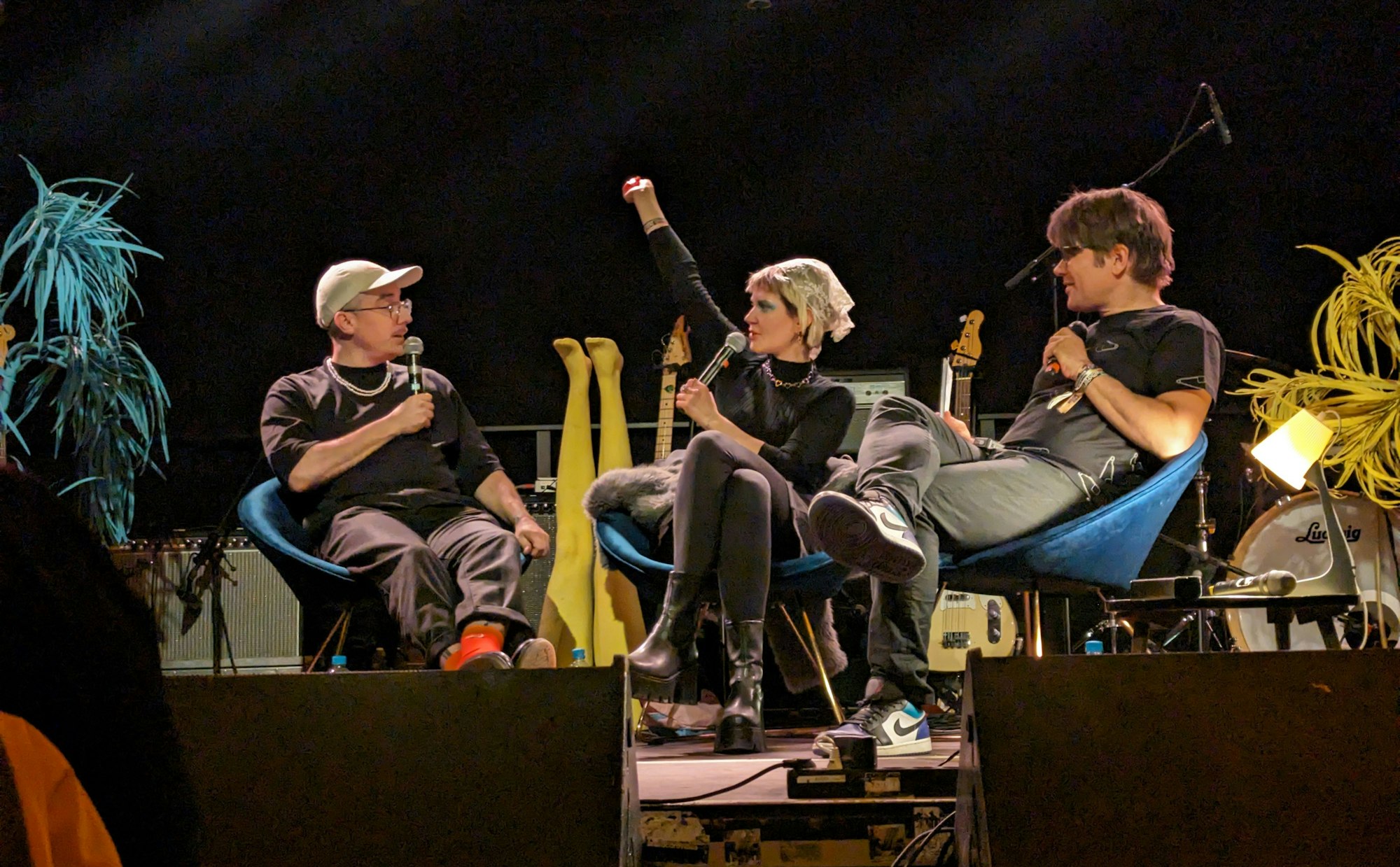 Drei Menschen sitzen auf einer Bühne, sie haben Mikrofone in der Hand und sprechen miteinander.