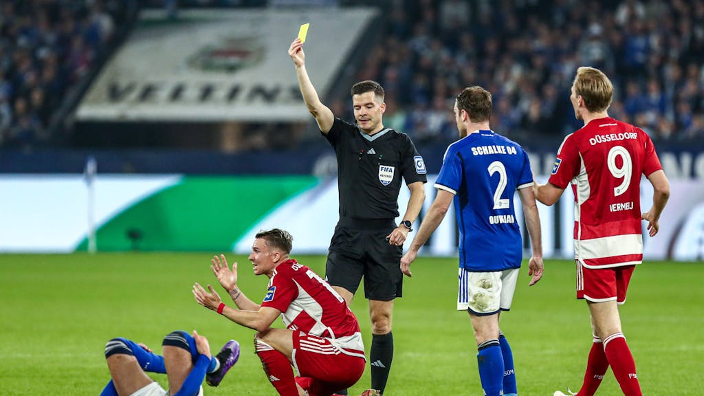 Fortuna Düsseldorfs Felix Klaus kniet am Boden, Schiedsrichter Harm Osmers zeigt ihm die Gelbe Karte.
