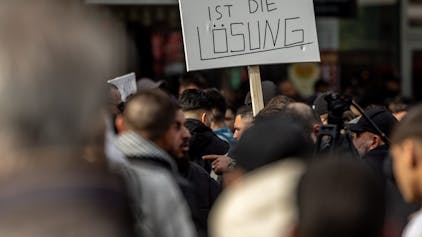 Teilnehmende einer Islamisten-Demo halten ein Plakat mit der Aufschrift „Kalifat ist die Lösung“ in die Höhe, hier im April 2024.