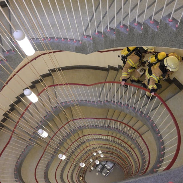 Blick von oben hinunter in ein Treppenhaus, das oval geschwungen über acht Etagen nach unten verläuft.