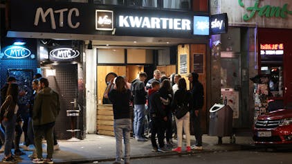 Fassade mit Bars und Clubs, davor stehen trinkende Menschen.