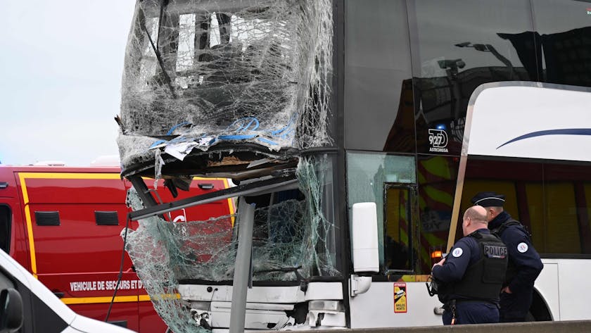 Das Bild zeigt einen Bus, der nach einer Kollision stark beschädigt ist. Zwei Polizisten schauen sich den Bus an.