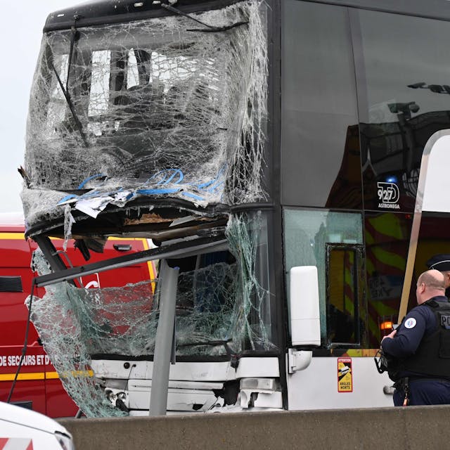 Das Bild zeigt einen Bus, der nach einer Kollision stark beschädigt ist. Zwei Polizisten schauen sich den Bus an.