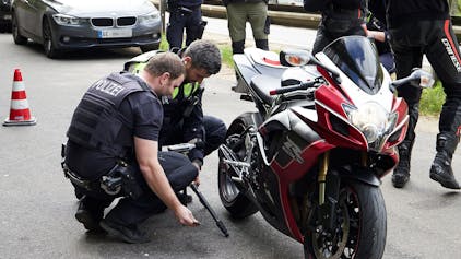Zwei Polizisten hocken neben einem Motorrad und begutachten die Auspuffanlage.