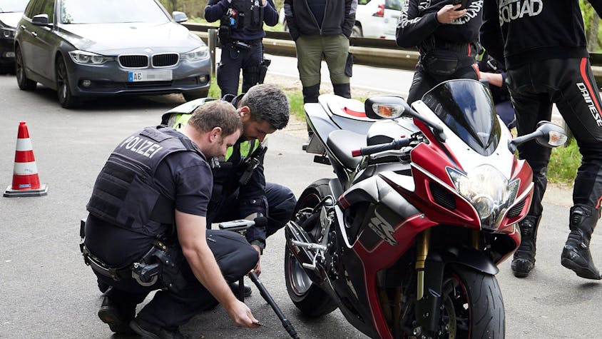 Zwei Polizisten hocken neben einem Motorrad und begutachten die Auspuffanlage.