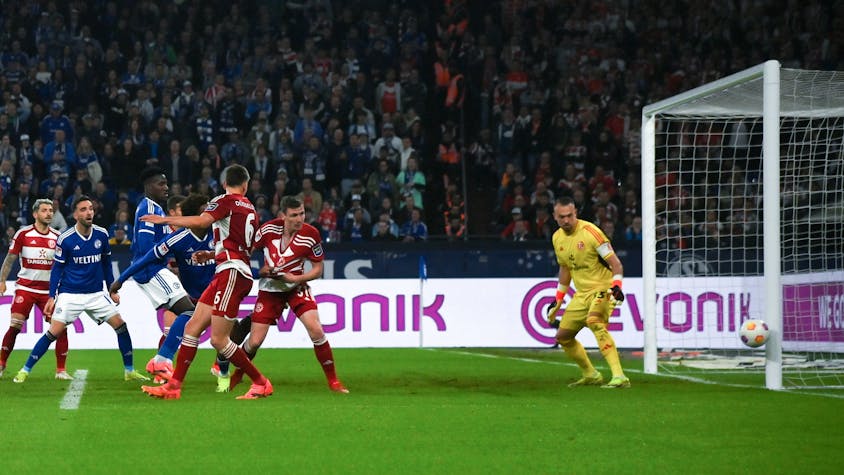 Fortuna Düsseldorf und Schalke 04 Spieler schauen auf den Ball, der den Pfosten vom Tor trifft.