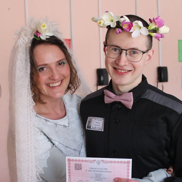 Evgenia Kulakova undViktor Filinkov, sie mit weißem Schleier, er mit Blumenkranz im Haar, bei der Hochzeit im Gefängnis. Beide lachen.