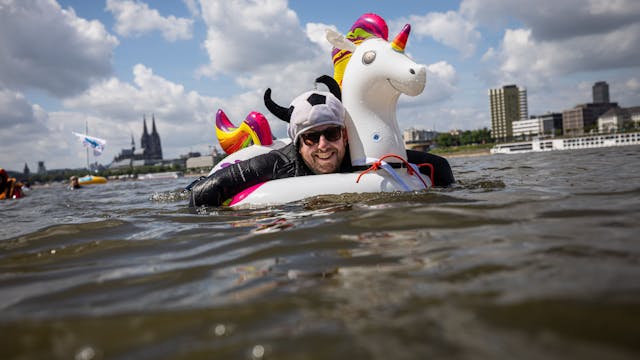 Ein kostümierter Teilnehmer schwimmt im Rhein am Panorama der Stadt mit dem Kölner Dom vorbei.&nbsp;
