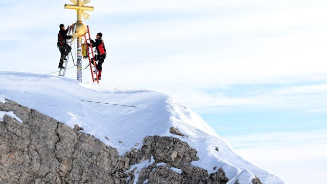 Zwei Personen bringen die im Tal restaurierten Strahlen des Gipfelkreuzes der Zugspitze wieder an.&nbsp;