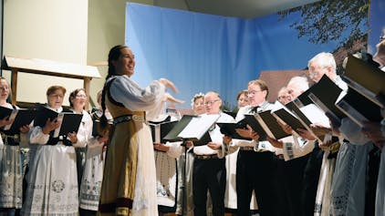 Sängerinnen und Sänger in Tracht gruppieren sich um ihre Dirigentin.