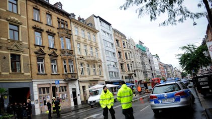 Polizisten und Feuerwehrleute stehen am 12.09.2013 auf der Aachener Straße in Köln (Nordrhein-Westfalen) vor einem einsturzgefährdeten Haus (weißes Erdgeschoss).