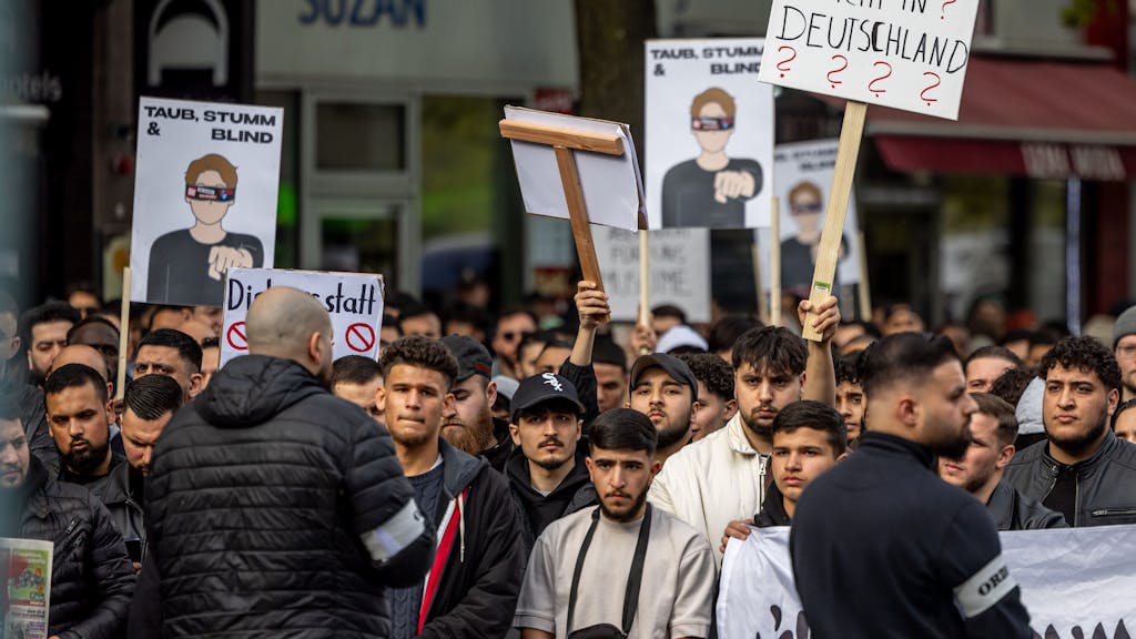 Teilnehmende einer Islamisten-Demo in Hamburg halten am Samstag (27. April 2024) ein Plakat mit der Aufschrift  „Andersdenken? Nicht in Deutschland“ in die Höhe.
