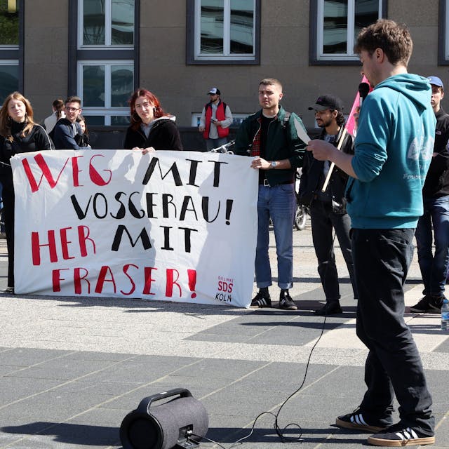 Studierende demonstrieren auf dem Albertus-Magnus-Platz. Auf einem Plakat steht: „Weg mit Vosgerau! Her mit Fraser!“