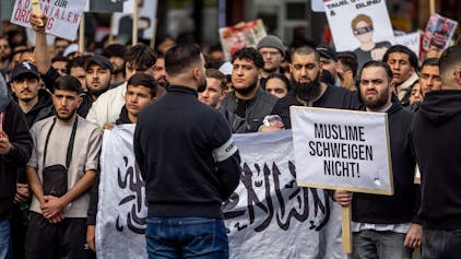 Teilnehmer einer Islamisten-Demo in Hamburg halten am Samstag ein Plakat mit der Aufschrift ·Muslime schweigen nicht in die Höhe.