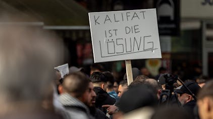 27.04.2024, Hamburg: Teilnehmer einer Islamisten-Demo halten ein Plakat mit der Aufschrift ·Kalifat ist die Lösung· in die Höhe.&nbsp;