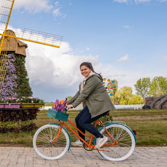 Eine Frau fährt auf dem Fahrrad vor einer Windmühle, die mit Blüten besteckt ist.&nbsp;