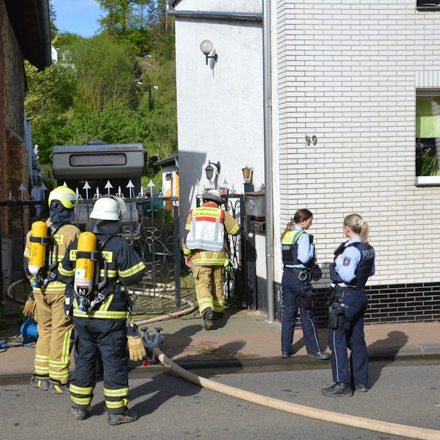 Feuerwehrleute und zwei Polizistinnen stehen vor dem Haus in der Hauserbachstraße.